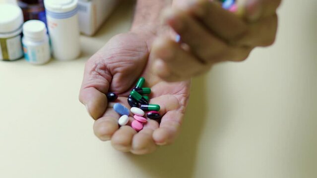 Unrecognizable studio isolated senile hands pour multi-colored medical pills from hand to hand.