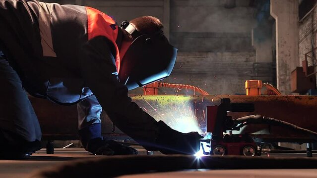 Male professional welder in overalls and in a mask welds metal plates or metal parts with the help of professional tools at the factory or construction