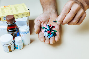 Unrecognizable hand holds handful of pills, other hand takes one tablet, super dose.