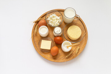 Beautiful rustic still life with organic farm dairy products on wooden tray. Flat lay on milk, yogurt, cottage cheese, butter, cheese, curd and eggs on white table. Top view, mock up, copy space