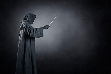 Wizard with hooded cape and magic wand over dark misty background