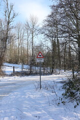Road in the winter forest with a warning sign on the road.
