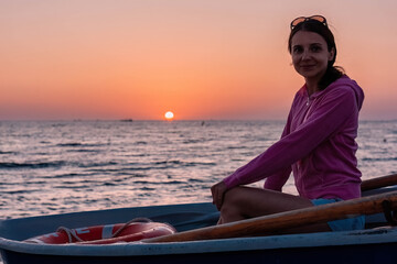 Woman sitting in boat in sea against the background of sunset