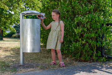 A little girl throws trash into a street trash can
