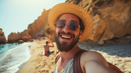 Cheerful man with a beard is taking a selfie at the beach, wearing a straw hat and sunglasses