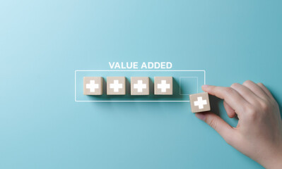 Value add concept. Hand place wooden cube with plus sign on light blue background. Positive...