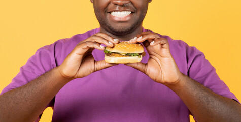 Cropped Shot Of Black Guy Holding Burger Over Yellow Background
