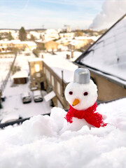 Small snowman in a red scarf against the backdrop of a winter city