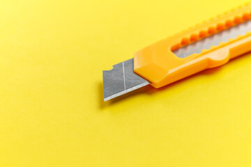 A utility knife with a retractable segmented blade on a creative yellow background