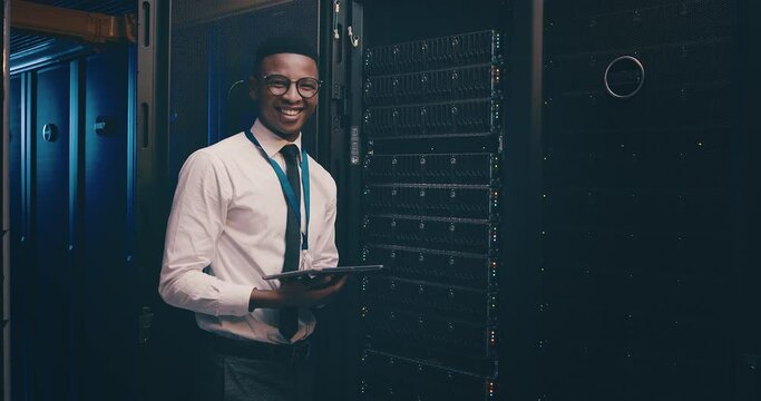 Portrait of black man in data center with tablet, inspection or network maintenance with engineer in storage update. Tech, system administration or happy technician on digital app in server room.