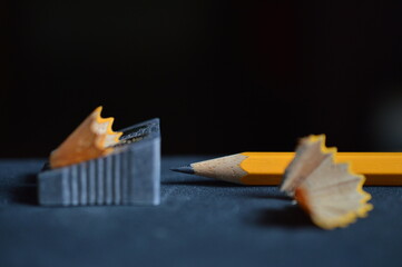 close up of pencil shavings, pencil sharpener and pencil on dark gray 