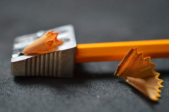 close up of pencil shavings, pencil sharpener and pencil on dark gray 
