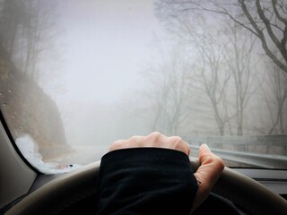 Hand on the steering wheel and fog seen from the car windshield 