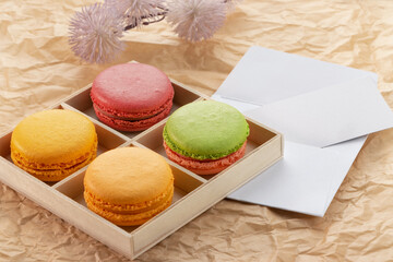 Multicolored macarons in a wooden box on paper with a note