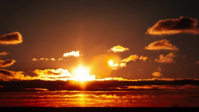 Sunset above the horizon in orange sky with soft clouds, timelapse. 4K. Bright sun setting down above the horizon. Epic, vibrant color. Time lapse. Sundown.