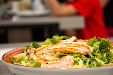 close up of salad plate with healthy grilled chicken breast in restaurant blurred background