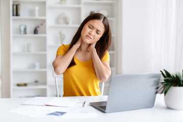 Asian freelancer woman feeling neck pain while working at her laptop