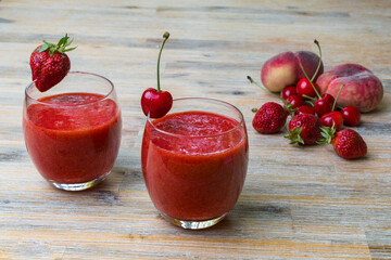 Two glasses of strawberry smoothie on a wooden table, on the glasses there are cherries and...
