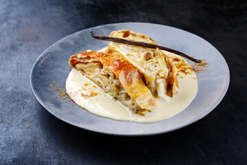 Traditioneller bayerischer Apfelstrudel mit gebackenen Äpfeln, Rosinen und Vanillesoße serviert als Nahaufnahme auf einem Design Teller