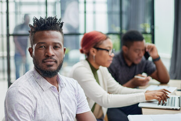 young African American man posing for the camera while sitting at a table in front of his colleagues