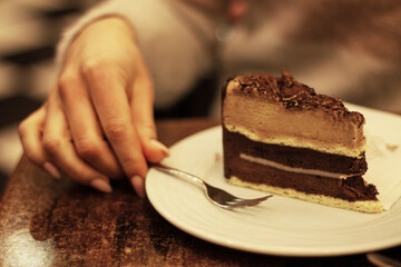 piece of chocolate cake on a white plate female hand holding a fork
