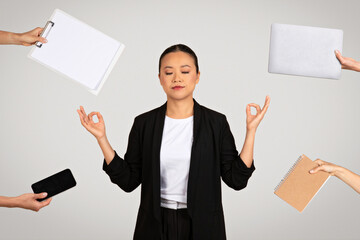 Serene Asian businesswoman in a meditative pose surrounded by office items