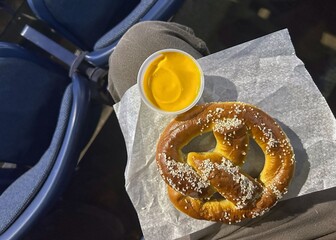 A giant pretzel and cheese balancing on a patrons leg demonstrating the challenge of eating in an arena