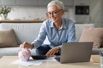 woman with piggybank putting coin managing funds near laptop indoor - Powered by Adobe