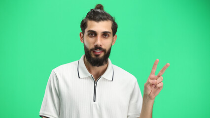 Naklejka premium A man, close-up, on a green background, shows a victory sign