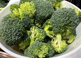 A white bowl of green, raw broccoli florets