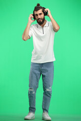 A man, full-length, on a green background, listening to music with headphones