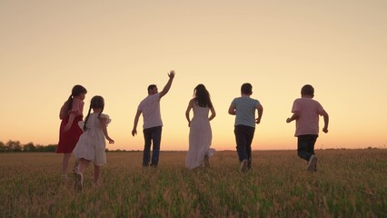 Family with children runs through grassy field in evening at sunset. Big family, group of people in...