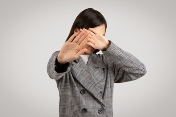 Young woman in houndstooth coat, covering face with hands