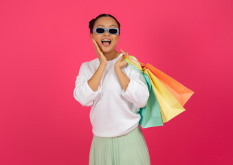 Surprised asian shopper lady in trendy sunglasses holding colorful shopping bags