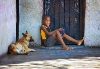 hungry african child with his dog having lunch in front of the door