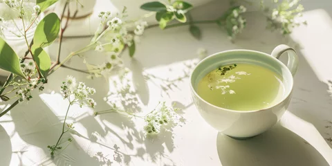 Fotobehang Moringa Flower Tea in Serene Morning Light on white table. A cup of soothing moringa flower tea surrounded by delicate blossoms in soft sunlight. © dinastya