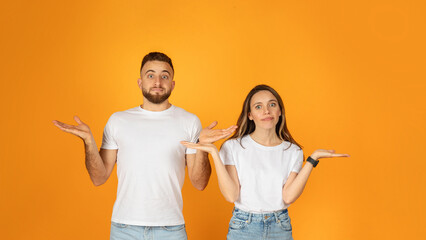 Confused young couple in white t-shirts and denim jeans shrugging with hands
