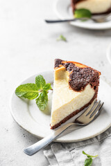 Piece of homemade chocolate cheesecake with mint leave on a plate on white textured background close up copy space