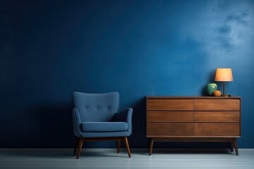  a blue chair next to a dresser with a lamp on top of it and a blue wall in the background.