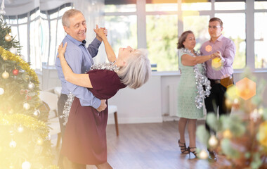 Aged man engaged in dance hall with mature female partner and dances Latin rumba during celebration...