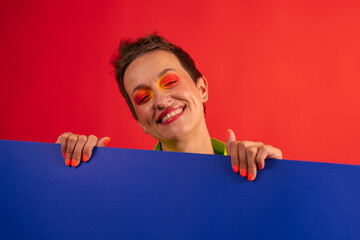 middle age woman with short haircut wear green overalls posing with cardboard on red background....