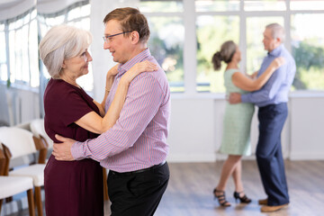 Smiling couple looking at each other while dancing slow dance in modern ballroom - obrazy, fototapety, plakaty