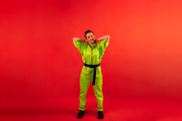 Full length body size photo of happy woman wear modern green overalls with paintbrush on bright red color background. energetic middle age female with colored make up having fun near copy space
