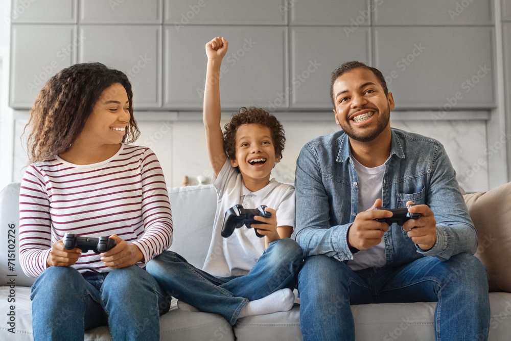 Wall mural family pastime. cheerful black parents playing video games with son at home