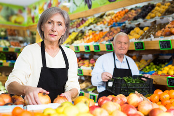 Obraz premium Woman merchandiser in apron putting goods on shelf in greengrocer