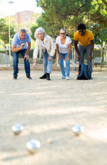 Portrait of mixed-race age-diverse mature men and women standing side by side with metal boules in...