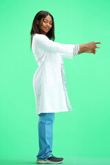 A female doctor, on a green background, in full height, points to the side