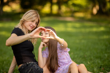 Obraz premium Mother and daughter making a heart shape with hands in the park