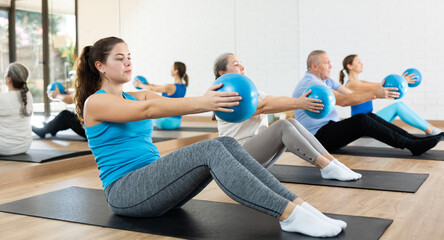 Sporty young girl doing sit-ups with bender ball to strengthen abs muscles during group pilates...