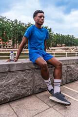 Young African American athlete dressed in blue sportswear resting and hydrating after the workout